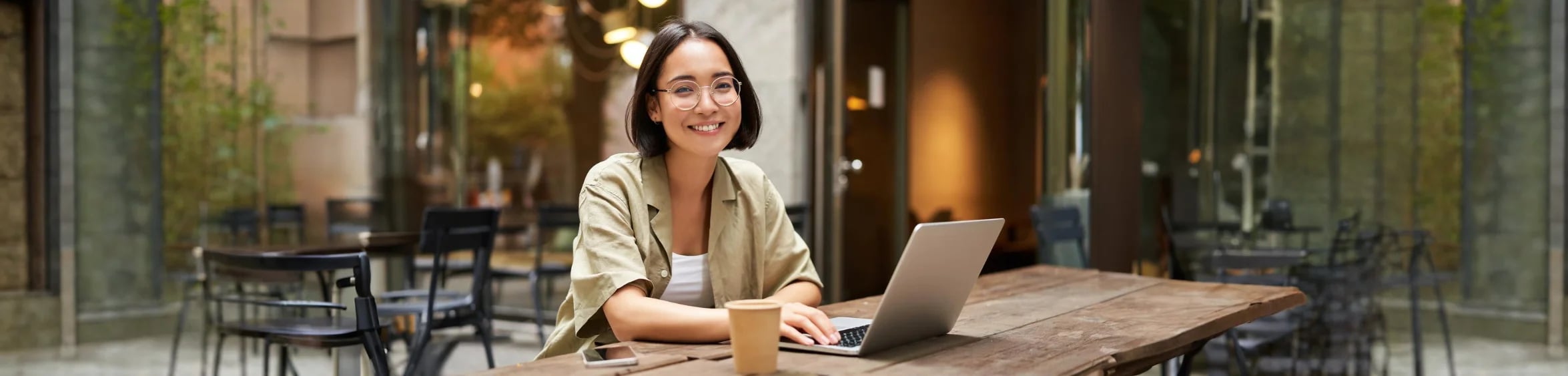 Presenter smiling on a live webinar broadcast from a laptop at an outdoor cafe table